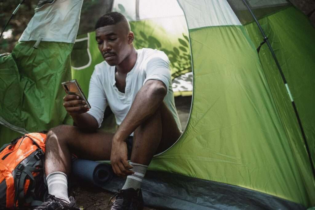 Backpacker sitting in his tent and looking at his cellphone. Photo by Kamaji Ogino.