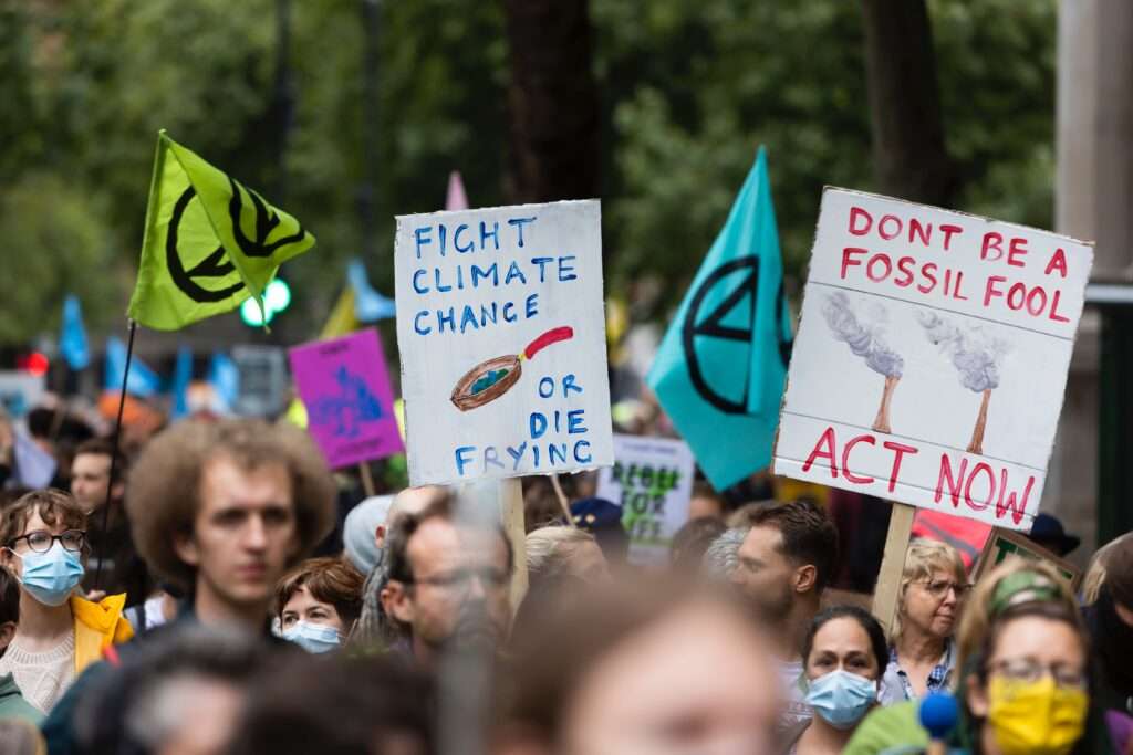 Crowd of people at a climate protest holding signs with slogans such as, "Fight climate change or die frying" and "Don't be a fossil fool. Act now."