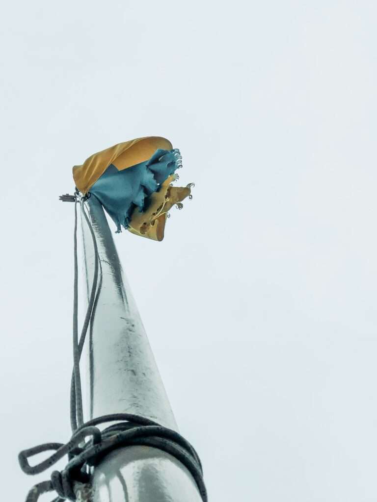 Tattered Ukrainian flag hanging from a flag pole in front of an overcast sky.