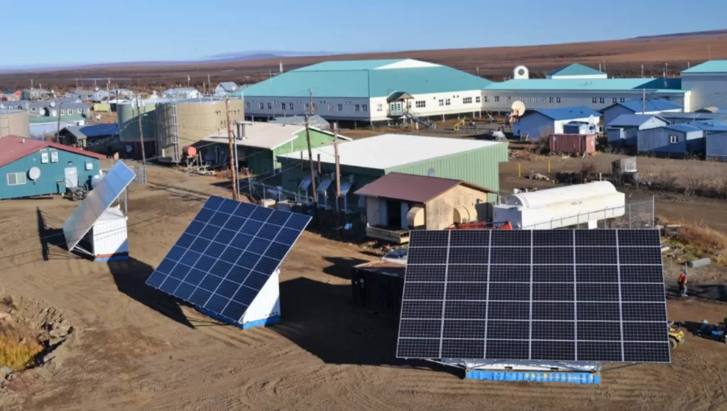 Small remote Alaskan town with 3 storage containers in the foreground. Each container has 42 solar panels attached to them that power the town.