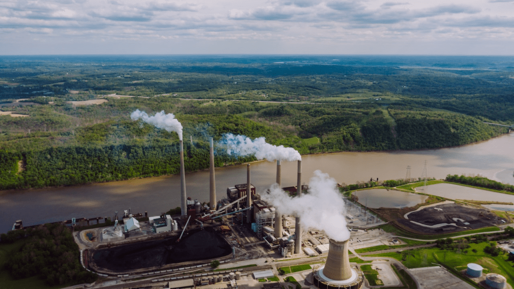 Coal power plant next to a river with fumes pouring out of 4 massive smokestacks.