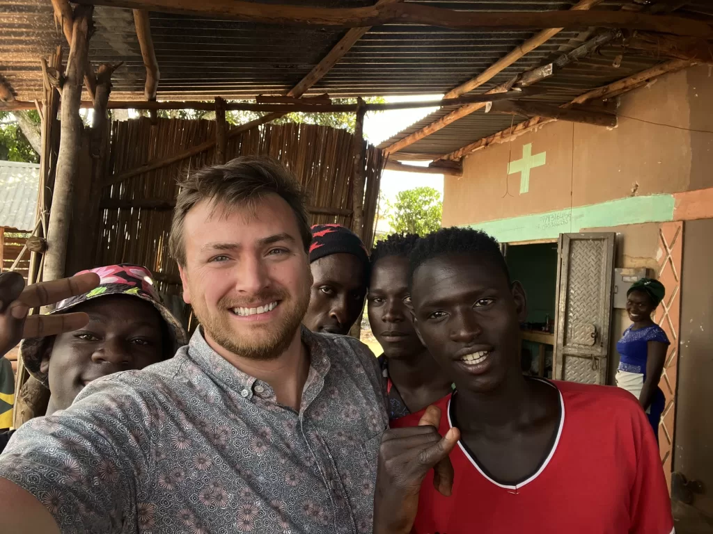 4 young men, a young lady, and Alexander Boom taking a selfie in front of a gaming center in the town of  Nakabululu.