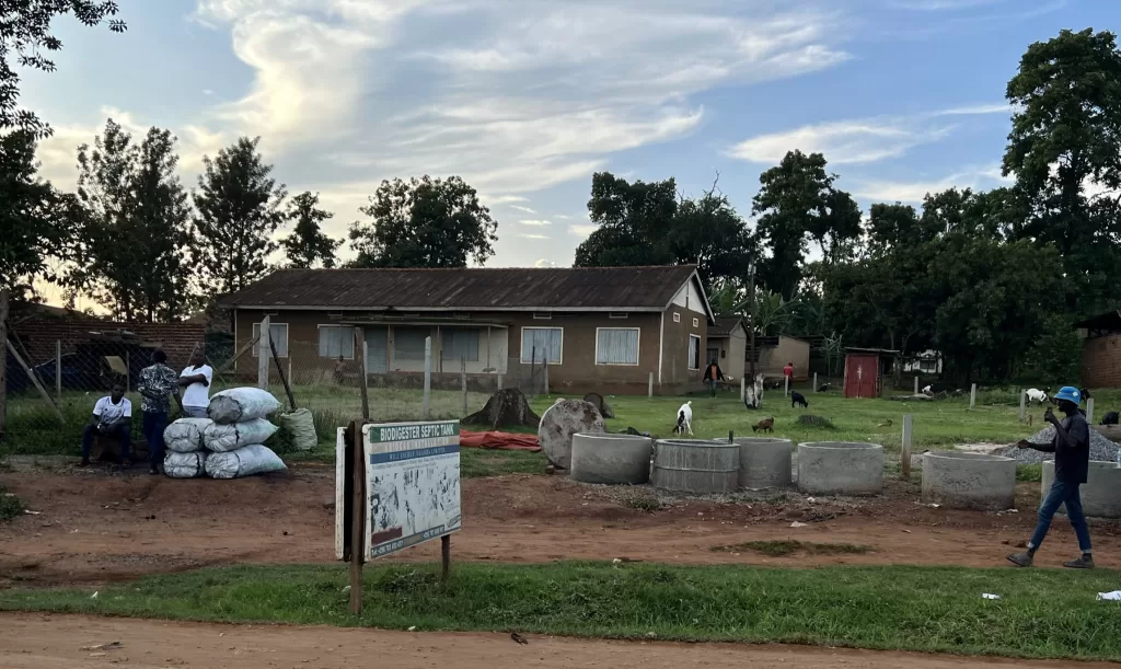 A roadside business selling cement biodigester septic tanks that produce energy. There are three men sitting by the tanks on display while a younger man walks by.