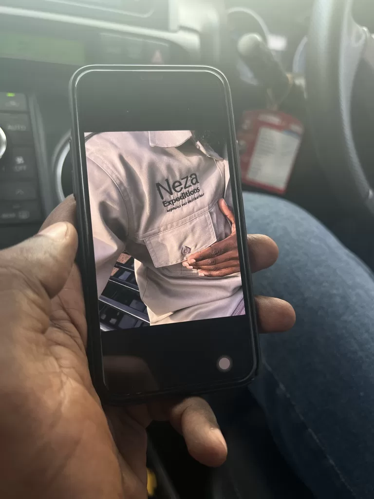 Hand holding a phone with a picture of Neza Expeditions logo on the shirt.