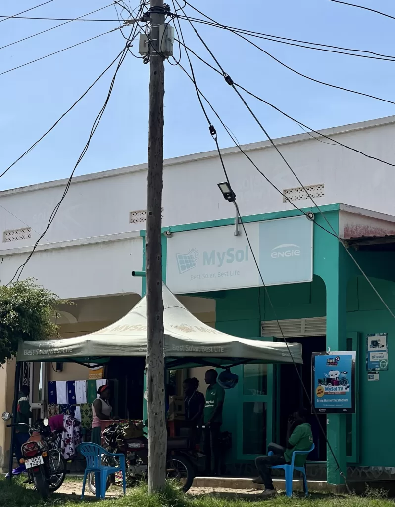 Storefront of MySol in Mbarara, Uganda. There's a tent out front of the store with MySol representatives speaking to potential customers about Ugandan solar energy.