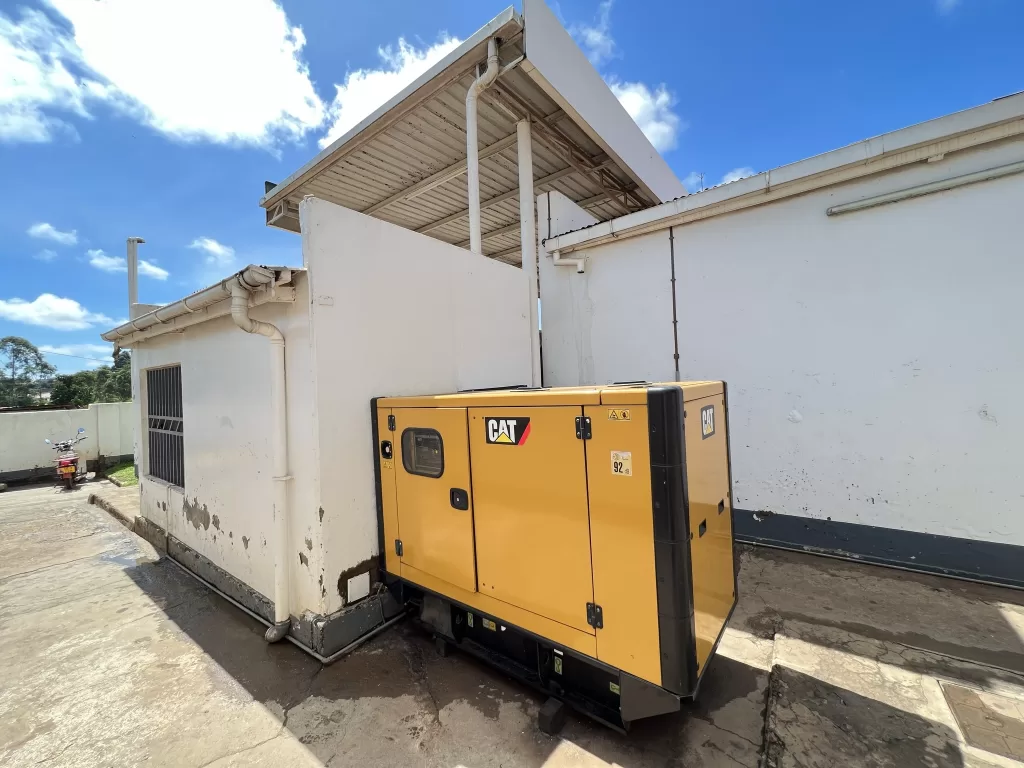 Yellow Cat (brand) diesel generator behind a large white facility.