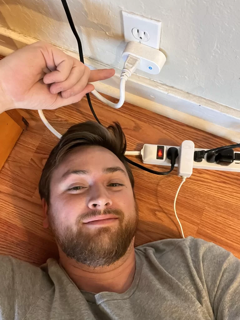 Alexander Boom lying on the ground, pointing at the smart outlet that connects the apartment to OhmConnect's virtual power plant.