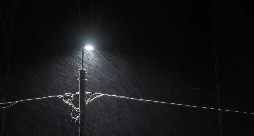 Snow falling at night on a street light and powerline.