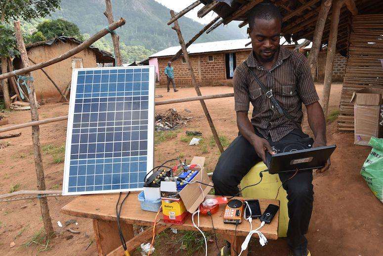 Man using a solar microgrid to charge cellphones and small devices with the most abundant Ugandan energy source, the sun.