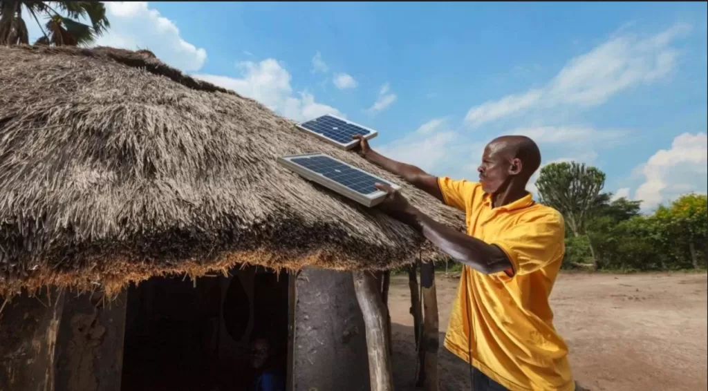 Ugandan man putting 2 solar panels on this thatched roof home so it's powered by a renewable microgrid.